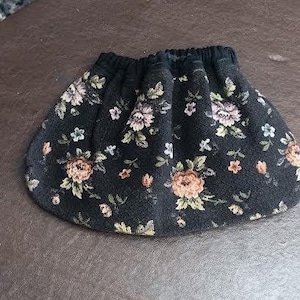 May include: A black skirt with a floral pattern featuring peach, pink, and white flowers with green leaves. The skirt has an elastic waistband and a gathered design, creating a full shape.