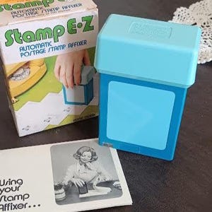 May include: A vintage Stamp E-Z automatic postage stamp affixer. The image shows the blue stamp affixer, its box, and an instruction sheet. The box is white and yellow with green text. The instruction sheet has a black and white photo.