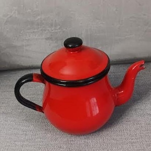 Puede incluir: Una tetera roja esmaltada con asa, boquilla y borde negros. La tapa tiene un pomo negro. Esta tetera de estilo vintage es un artículo de cocina clásico.