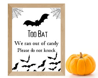 May include: A white sign with a black bat and the text "Too Bat. We ran out of candy. Please do not knock."  The sign is framed in wood and is sitting on a white surface.
