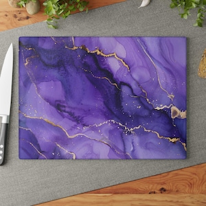 May include: Rectangular chopping board with a vibrant purple and gold abstract design. The board features shades of purple with gold accents, creating a marbled effect. The gold lines and specks add a touch of elegance to this kitchen accessory.