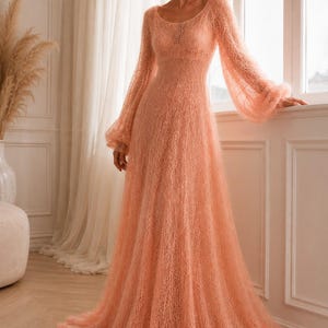 K&ouml;nnte beinhalten: Ein bodenlanges pfirsichfarbenes Kleid mit transparenter, grob gestrickter Textur, rundem Ausschnitt und langen, volumin&ouml;sen Bischofs&auml;rmeln, die an den Handgelenken gerafft sind. Das Kleid hat ein eng anliegendes Oberteil und einen weiten Rock.