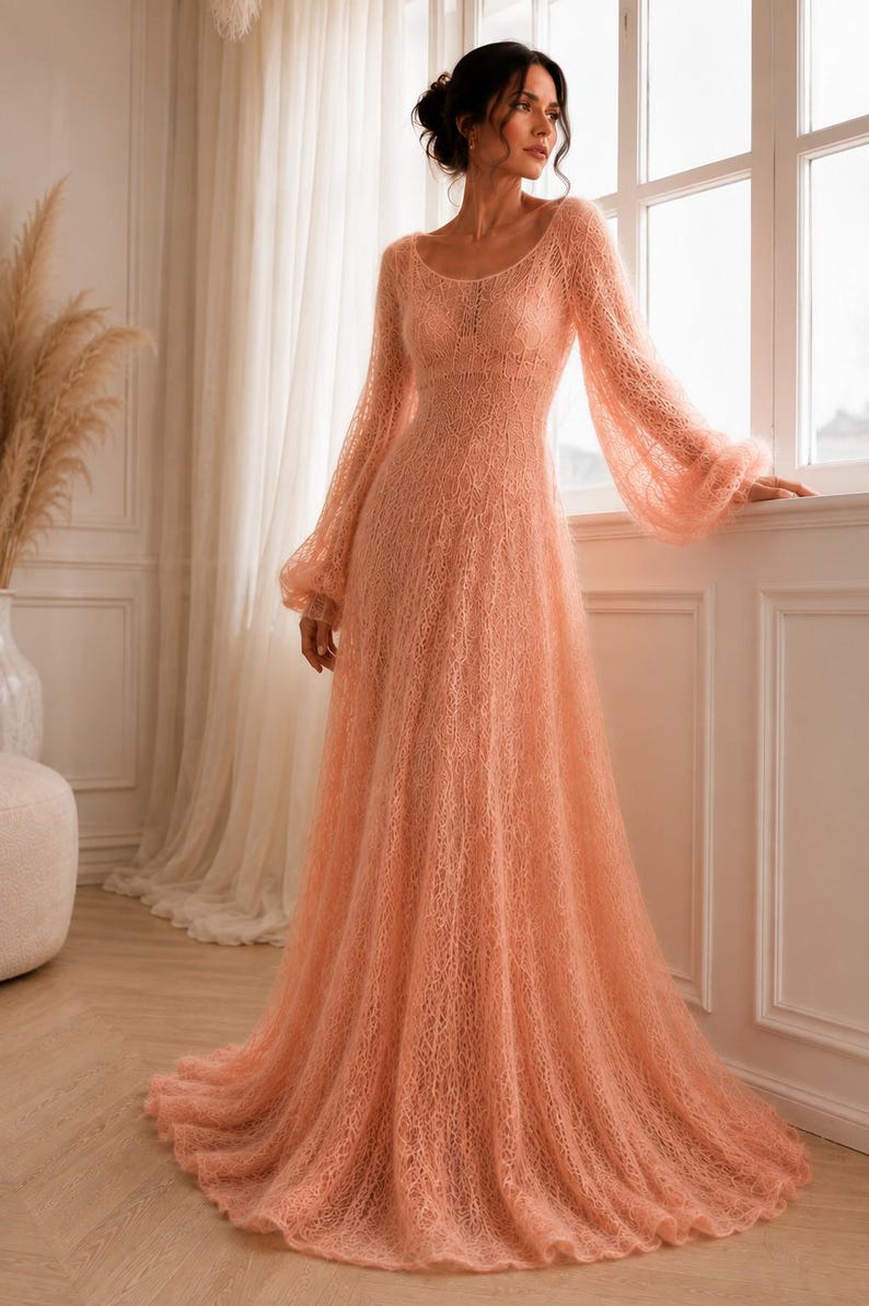 K&ouml;nnte beinhalten: Ein bodenlanges pfirsichfarbenes Kleid mit transparenter, grob gestrickter Textur, rundem Ausschnitt und langen, volumin&ouml;sen Bischofs&auml;rmeln, die an den Handgelenken gerafft sind. Das Kleid hat ein eng anliegendes Oberteil und einen weiten Rock.