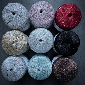 Op de afbeelding: Tien spoelen garen met pailletten, in verschillende kleuren, waaronder zilver, goud, roze, rood, zwart en blauw.