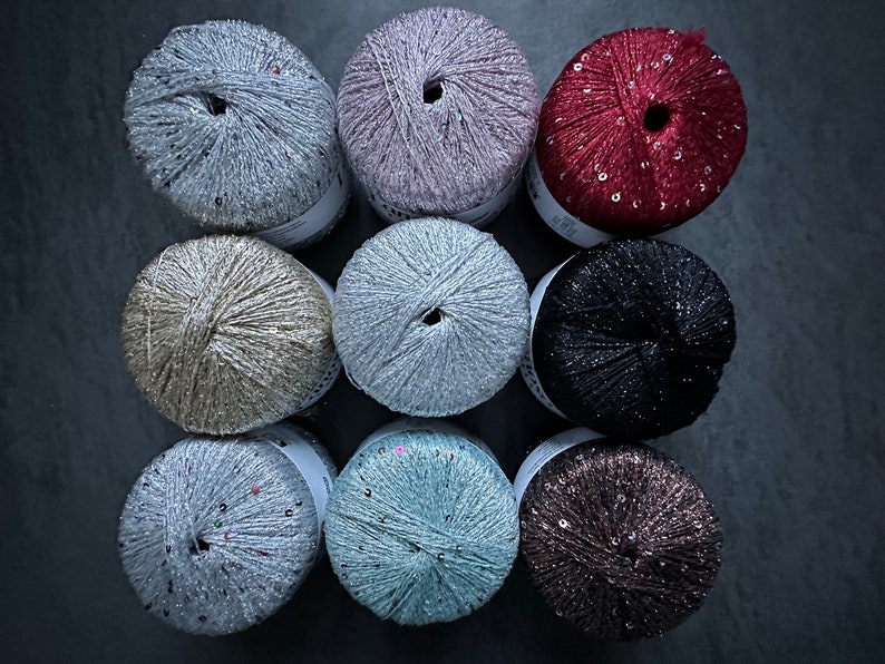 Op de afbeelding: Tien spoelen garen met pailletten, in verschillende kleuren, waaronder zilver, goud, roze, rood, zwart en blauw.