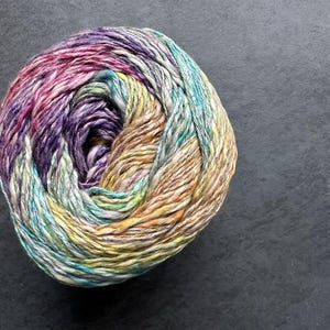 Puede incluir: Una bola de hilo con un patr&oacute;n multicolor y jaspeado en tonos de rosa, morado, amarillo, verde y azul.
