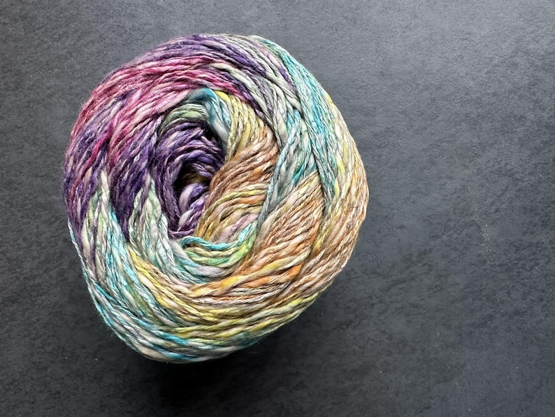 Puede incluir: Una bola de hilo con un patr&oacute;n multicolor y jaspeado en tonos de rosa, morado, amarillo, verde y azul.