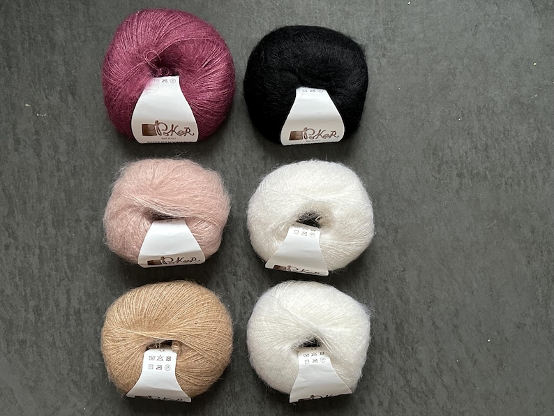 K&ouml;nnte beinhalten: Sechs runde Kn&auml;uel aus flauschigem Garn, angeordnet in zwei Spalten. Die Farben umfassen tiefes Magenta, Schwarz, zartes Rosa sowie drei Wei&szlig;- und Beiget&ouml;ne. Jedes Kn&auml;uel hat ein wei&szlig;es Papieretikett mit dem aufgedruckten Text Poker.