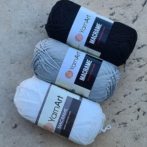 May include: Three balls of yarn in white, grey, and black. Each ball has a label that says "YarnArt Macrame" and a website address.