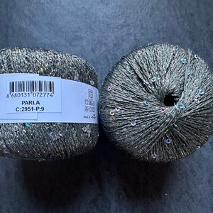 Op de afbeelding: Twee bollen zilver en grijs garen met iriserende pailletten. Het etiket vermeldt "PARLA C:2951-P-9 8 680131 072774"