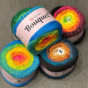 以下が含まれることがあります： 虹色のグラデーションパターンで4つの糸巻き。糸は「YarnArt Bouquet」と「Easy Soft」とラベル付けされています。