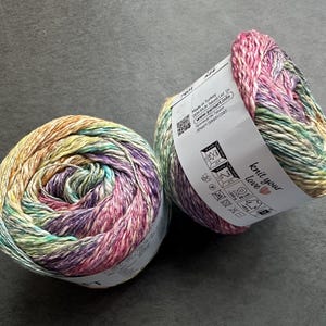 Puede incluir: Dos ovillos de hilo en un color arco&iacute;ris. El hilo es una mezcla de algod&oacute;n y lino. La etiqueta dice "Knit your love" con un coraz&oacute;n.