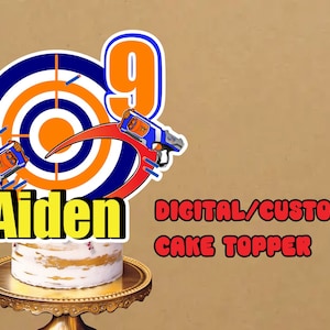 May include: A digital cake topper featuring a blue and orange target with a red crescent moon, two blue and orange toy guns, and the name "Aiden" in yellow letters. The text "DIGITAL/CUSTOMISE CAKE TOPPER" is also included.