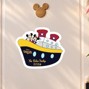 May include: A sticker featuring a Disney Dream cruise ship with Mickey and Minnie Mouse on the deck. The ship is navy blue, yellow, and white with red smokestacks. Text on the ship reads Disney Dream, The Slinn Family, and the year 2026.