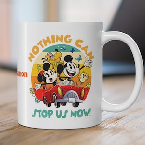 Może przedstawiać: Biały ceramiczny kubek z kolorową kreskówkową grafiką Myszki Miki i Myszki Minnie w czerwonym samochodzie, z napisem "NOTHING CAN STOP US NOW!". Projekt zawiera żółte, pomarańczowe i niebieskie akcenty w stylu retro.