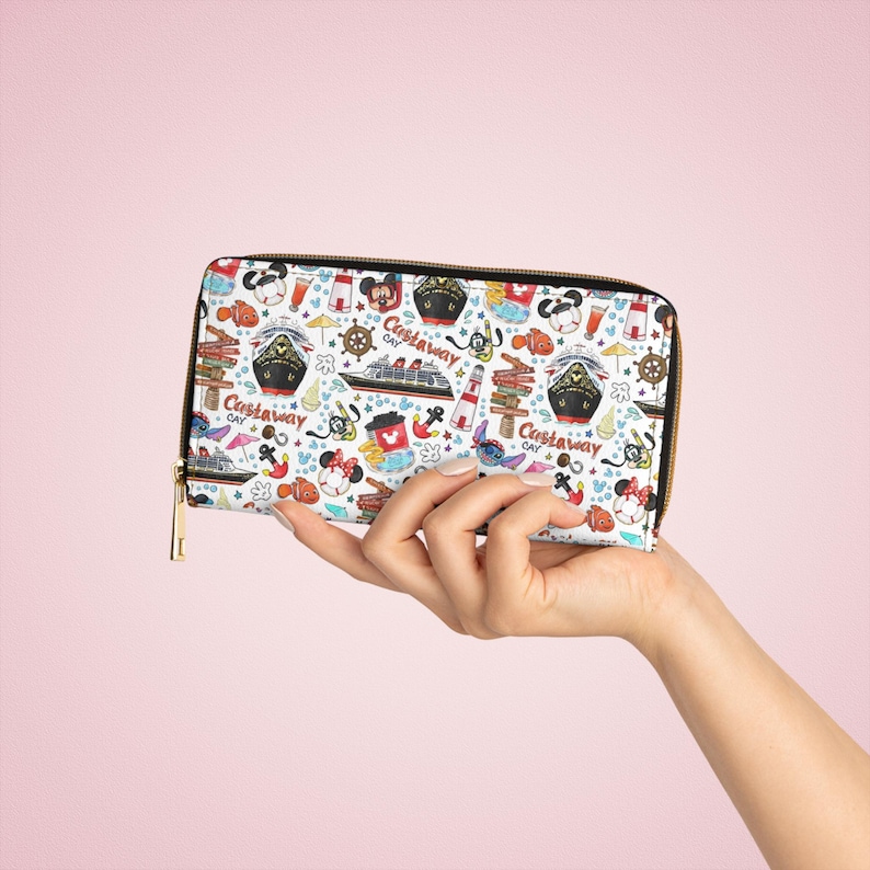 May include: A white zippered wallet with a colourful print of Disney characters and nautical themed designs. The print includes Mickey Mouse, Minnie Mouse, Stitch, and a cruise ship. The text "Castaway Cay" is repeated throughout the print.