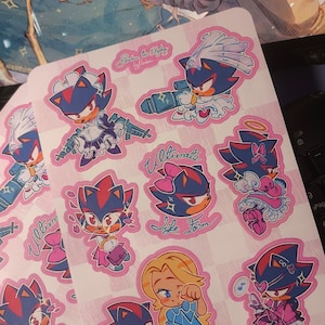 Puede incluir: Una colección de pegatinas rosas y blancas con varios personajes de dibujos animados en diferentes poses. Algunas pegatinas tienen el texto "Ultimate Life Form". Las pegatinas están sobre una superficie estampada, con un teclado de portátil visible en el fondo.