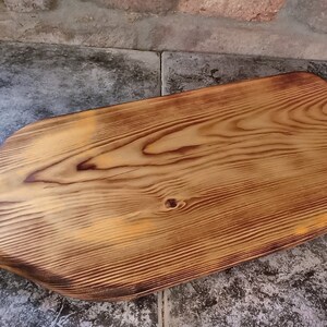 May include: A large, rectangular wooden chopping board with a handle. The board has a natural wood finish and is made of light brown wood. The handle has a hole in it for hanging.