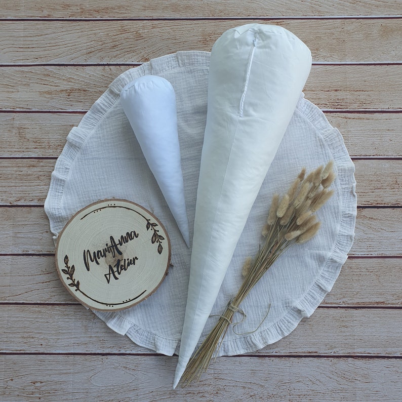 Op de afbeelding: Twee witte stoffen kegels op een witte mousseline achtergrond met een houten bord met de tekst "Marija Anna Atelier".
