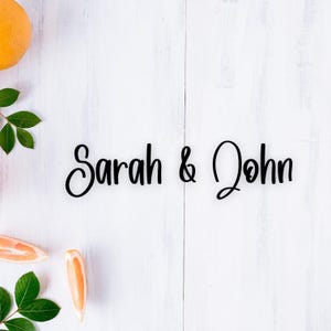 May include: A white wooden background with the text "Sarah & John" written in black cursive script. There are citrus fruits and green leaves on the left and right sides of the image.