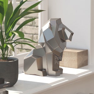 Op de afbeelding: Een zilveren geometrisch leeuwenbeeld staat op een vensterbank met een potplant en boeken. Het beeld is gemaakt van veel kleine driehoeken en heeft een moderne, abstracte stijl.
