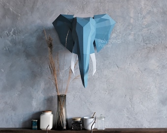 May include: A blue geometric paper elephant head mounted on a gray wall. The elephant has large ears and white tusks. The text "Polygonal Paper" is visible on the right side of the elephant. A vase with dried plants and other decorative items are on a wooden shelf below.