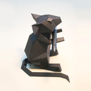 May include: A black papercraft mouse holding a black pen. The mouse is sitting on a white surface. The text "Polygonal Paper" is visible in the lower left corner of the image.