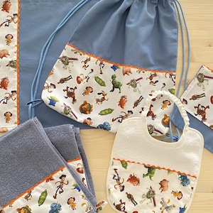 Könnte beinhalten: Eine Sammlung von Babyartikeln mit einem blau-weißen Muster mit Zeichentrickfiguren. Das Set umfasst eine Lätzchen, Handtücher, einen Kordelzugbeutel und eine Wickelauflage. Die Kanten sind mit orangefarbenem, gewelltem Stoff verziert.