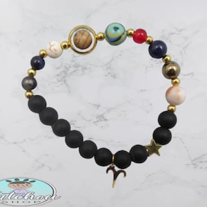 Peut inclure: Un bracelet en perles noires avec des accents dorés, un charme doré du signe du zodiaque Bélier et un charme d'étoile dorée. Le bracelet comprend également une variété de perles colorées, notamment bleues, rouges, blanches et brunes.