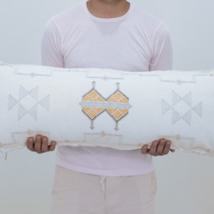 May include: A white rectangular pillow with a geometric pattern in gray and yellow. The pillow has tassels on each end.