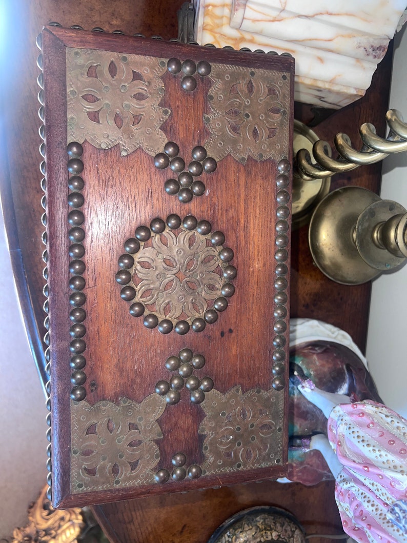 Op de afbeelding: Een houten kist met messing accenten. De kist is versierd met ingewikkelde bloemmotieven en heeft een rand van metalen studs.