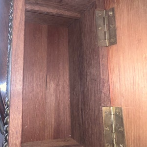 Op de afbeelding: De binnenkant van een houten doos met twee messing scharnieren. De doos is gemaakt van donker hout en heeft een natuurlijke afwerking. De scharnieren zijn bevestigd aan het deksel van de doos en zijn zichtbaar wanneer het deksel open is.