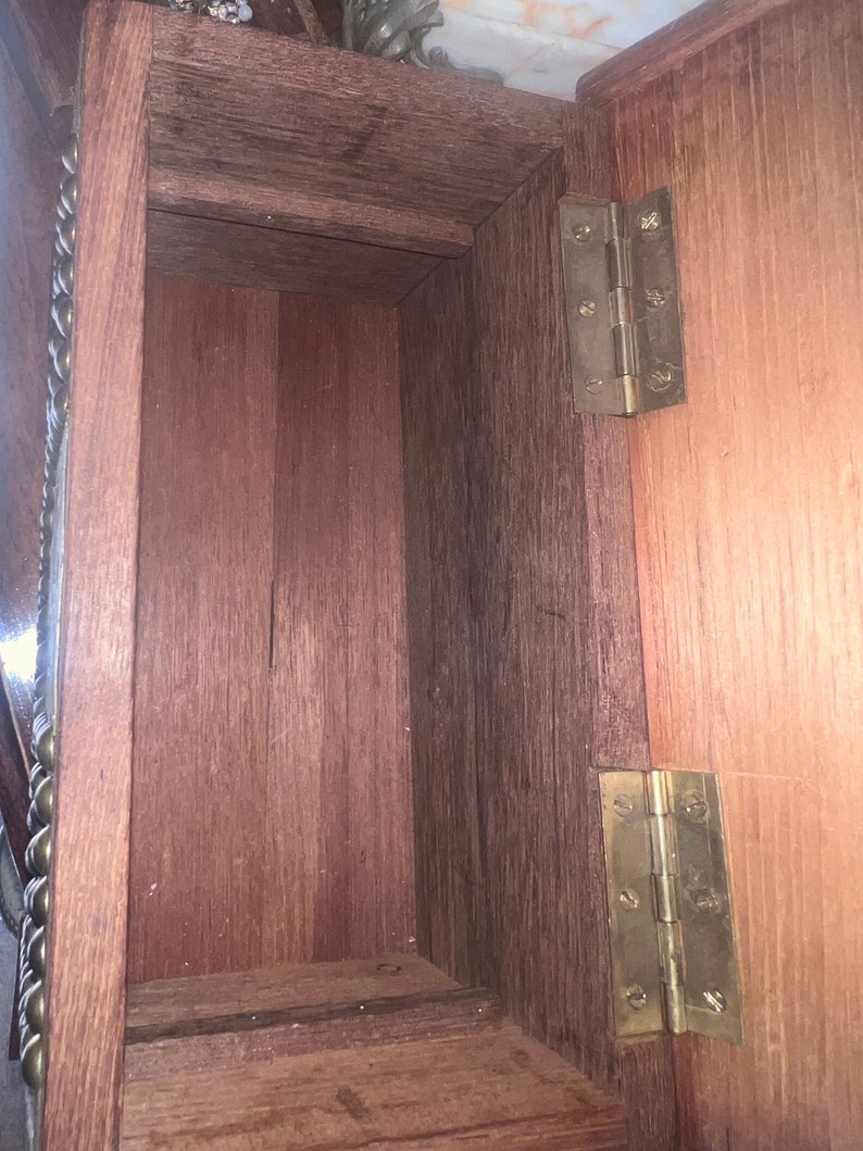 Op de afbeelding: De binnenkant van een houten doos met twee messing scharnieren. De doos is gemaakt van donker hout en heeft een natuurlijke afwerking. De scharnieren zijn bevestigd aan het deksel van de doos en zijn zichtbaar wanneer het deksel open is.
