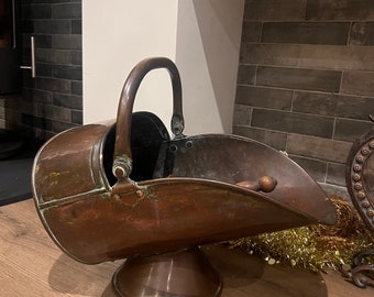 Può includere: Un secchio per carbone in rame vintage con un manico in legno e una base rotonda. Il secchio è leggermente inclinato e ha una finitura patinata.