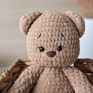 K&ouml;nnte beinhalten: Ein geh&auml;kelter brauner Teddyb&auml;r mit schwarzen gestickten Augen und einer braunen Nase. Der B&auml;r sitzt in einem Weidenkorb.