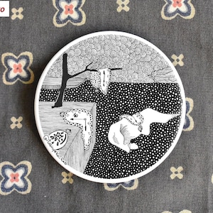 May include: Black and white ceramic coaster featuring a surrealist painting of a melting clock, a tree, and a floating elephant. The background is a swirling pattern of dots.