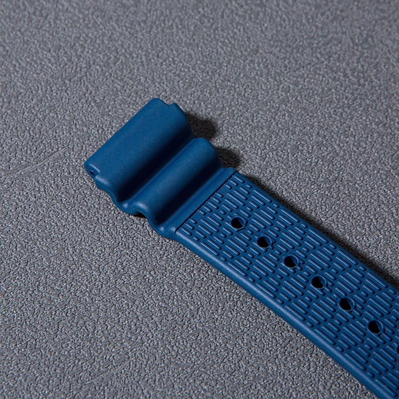 May include: A blue rubber watch strap with a textured pattern and multiple holes for adjusting the size.
