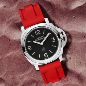 May include: A black-faced wristwatch with a red rubber strap. The watch face has white markings and the words "Luminor Panerai" printed on it.