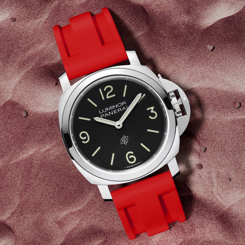 May include: A black-faced wristwatch with a red rubber strap. The watch face has white markings and the words "Luminor Panerai" printed on it.