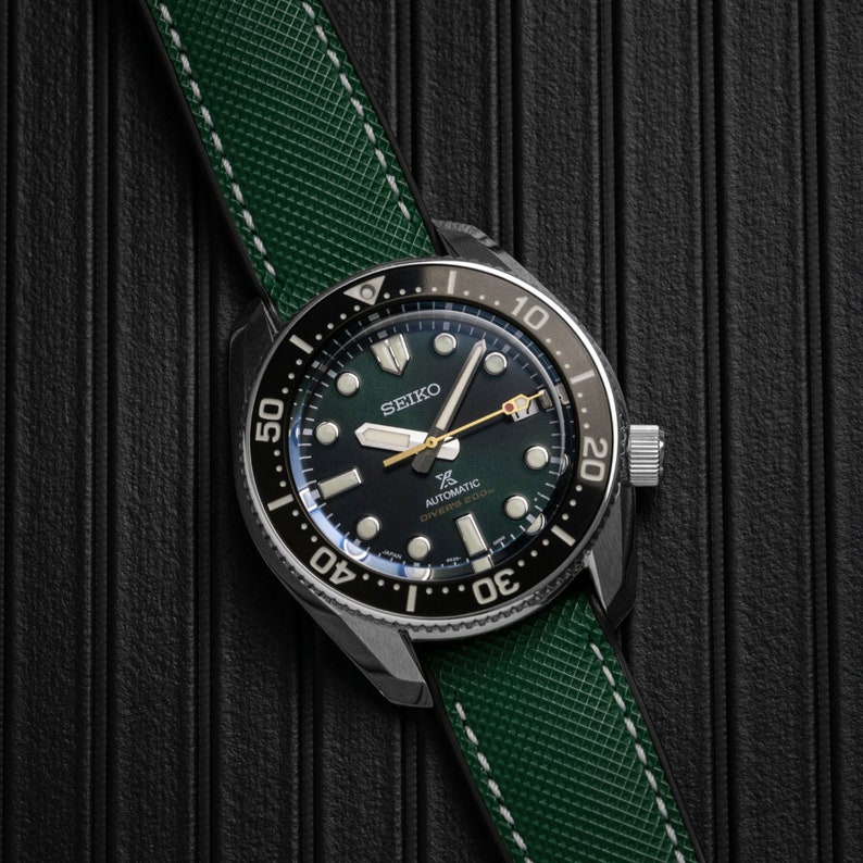 Puede incluir: Un reloj de pulsera negro y verde con una correa de cuero verde. La esfera del reloj tiene un fondo negro con marcas blancas y la palabra "SEIKO" en blanco. El reloj tambi&eacute;n tiene las palabras "AUTOMATIC" y "DIVER'S 200m" en blanco.