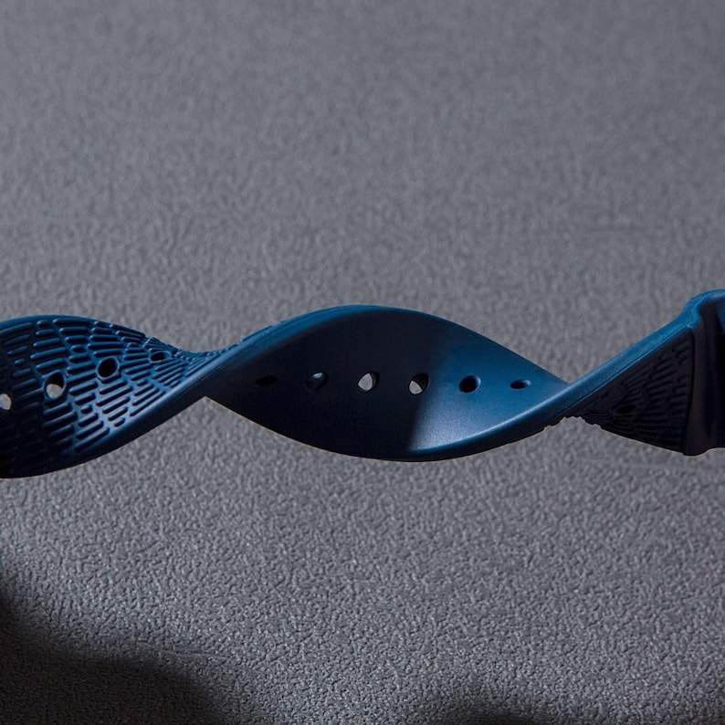 May include: A dark blue watch strap with a textured surface and multiple holes for adjusting the fit.