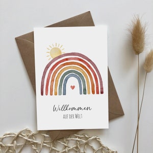 Postkarte auf braunem Umschlag aus Kraftpapier mit Motiv: Regenbogen mit aufgehender Sonne. Darunter der Text: Willkommen auf der Welt.