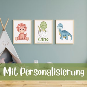 May include: Three watercolor dinosaur prints with a light blue, green, and red dinosaur. The prints are framed in wood and have a white background. The middle print has the name "Carlo" and a date written below it. The text "Mit Personalisierung" is written in green on a green background at the bottom of the image.