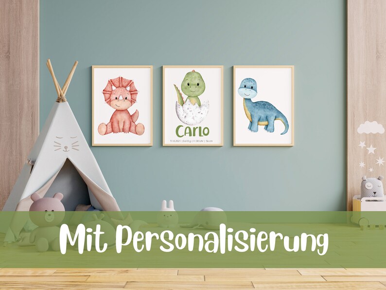May include: Three watercolor dinosaur prints with a light blue, green, and red dinosaur. The prints are framed in wood and have a white background. The middle print has the name "Carlo" and a date written below it. The text "Mit Personalisierung" is written in green on a green background at the bottom of the image.