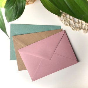 Drei Umschläge in Grün, Braun und Rosé, welche optional zur Postkarte dazu bestellt werden können.