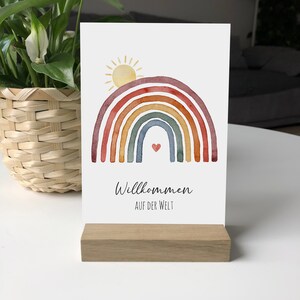 Postkarte mit Motiv: Regenbogen mit aufgehender Sonne. Darunter der Text: Willkommen auf der Welt