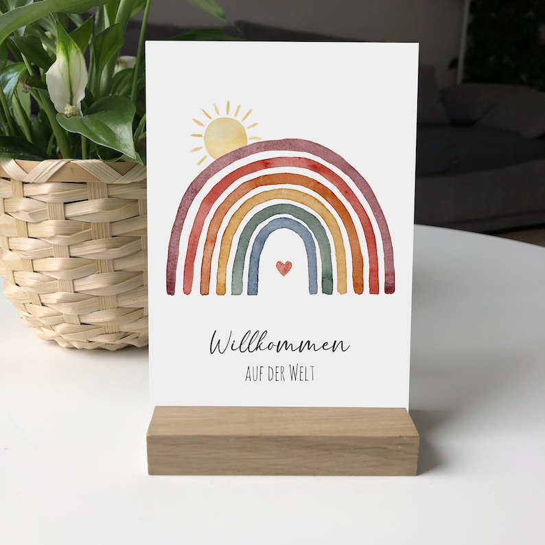 Postkarte mit Motiv: Regenbogen mit aufgehender Sonne. Darunter der Text: Willkommen auf der Welt