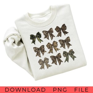 May include: A cream-colored crewneck sweatshirt featuring a graphic print of nine decorative bows arranged in a grid. The bows display various patterns including camouflage, leopard print, and solid brown tones with textured details on each bow.