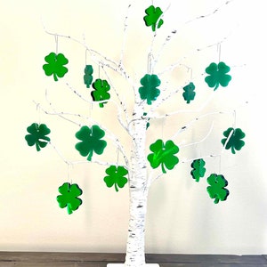 May include: A white birch tree with green shamrock ornaments hanging from the branches. The tree is on a wooden table.