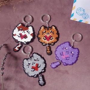 May include: Four colorful beaded cat keychains with red hearts. Each keychain features a different colored cat with a different colored tail.